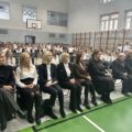 Na zdjęciu widoczne są osoby siedzące w sali gimnastycznej. Wśród nich znajdują się dyrekcja szkoły, przedstawiciele urzędu gminy oraz członkinie rady rodziców.