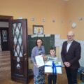 Na fotografii widoczny uczeń, który pozuje z nagrodą. Na fotografii także dyrektor szkoły w Buczu i kobieta.