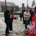 Zdjęcie przedstawia delegację składającą znicze i kwiaty przy pomniku, w obecności pocztu sztandarowego.